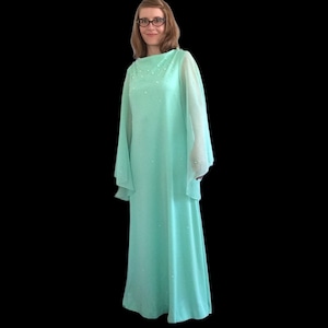 K&ouml;nnte beinhalten: Ein langes, flie&szlig;endes Kleid in Mintgr&uuml;n mit durchsichtigen, glockenf&ouml;rmigen &Auml;rmeln. Das Kleid ist mit kleinen, wei&szlig;en Verzierungen verziert.