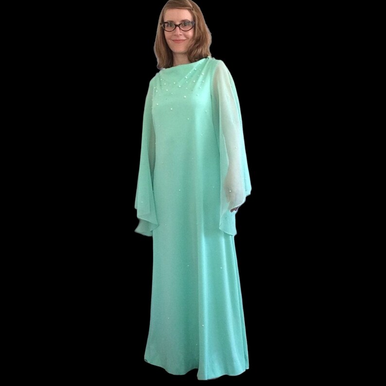 K&ouml;nnte beinhalten: Ein langes, flie&szlig;endes Kleid in Mintgr&uuml;n mit durchsichtigen, glockenf&ouml;rmigen &Auml;rmeln. Das Kleid ist mit kleinen, wei&szlig;en Verzierungen verziert.