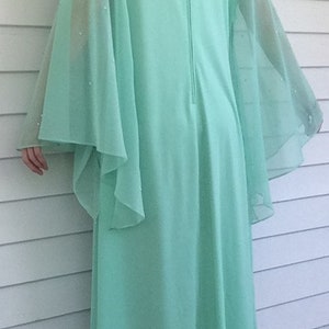 K&ouml;nnte beinhalten: Ein langes, flie&szlig;endes Maxikleid in Mintgr&uuml;n mit durchsichtigen, glockenf&ouml;rmigen &Auml;rmeln. Das Kleid hat einen Rei&szlig;verschluss auf der R&uuml;ckseite und ist aus einem weichen, leichten Stoff gefertigt.