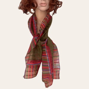 May include: A brown and red plaid scarf with a sheer texture. The scarf is tied around the neck in a loose knot.