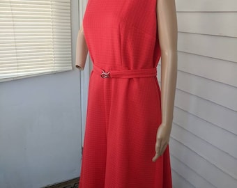 Könnte beinhalten: Ein ärmelloses, rotes, knielanges Kleid mit V-Ausschnitt und Gürtel. Das Kleid hat einen strukturierten Stoff und einen leicht ausgestellten Rock.