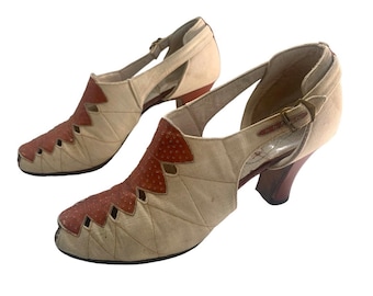 Op de afbeelding: Een paar beige canvas hakken met bruine leren accenten en uitsparingen. De schoenen hebben een band met een gesp bij de enkel.