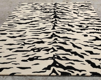May include: A rectangular rug with a cream-colored background and bold black stripes, creating a zebra-like pattern. The rug is laid out on a concrete floor, showcasing its design and texture. This rug is suitable for living rooms and bedrooms.