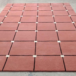 Peut inclure: Un tapis rectangulaire de couleur rose poudré avec un motif quadrillé. La grille est formée de lignes noires et de carrés blancs aux intersections. Le tapis est fait d'une matière douce et texturée.