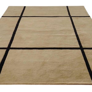 Könnte beinhalten: Ein rechteckiger beigefarbener Teppich mit einem Rastermuster aus dicken schwarzen Linien. Der Teppich hat eine weiche, plüschige Textur und eignet sich für ein Wohn- oder Schlafzimmer. Das Design ist modern und minimalistisch.