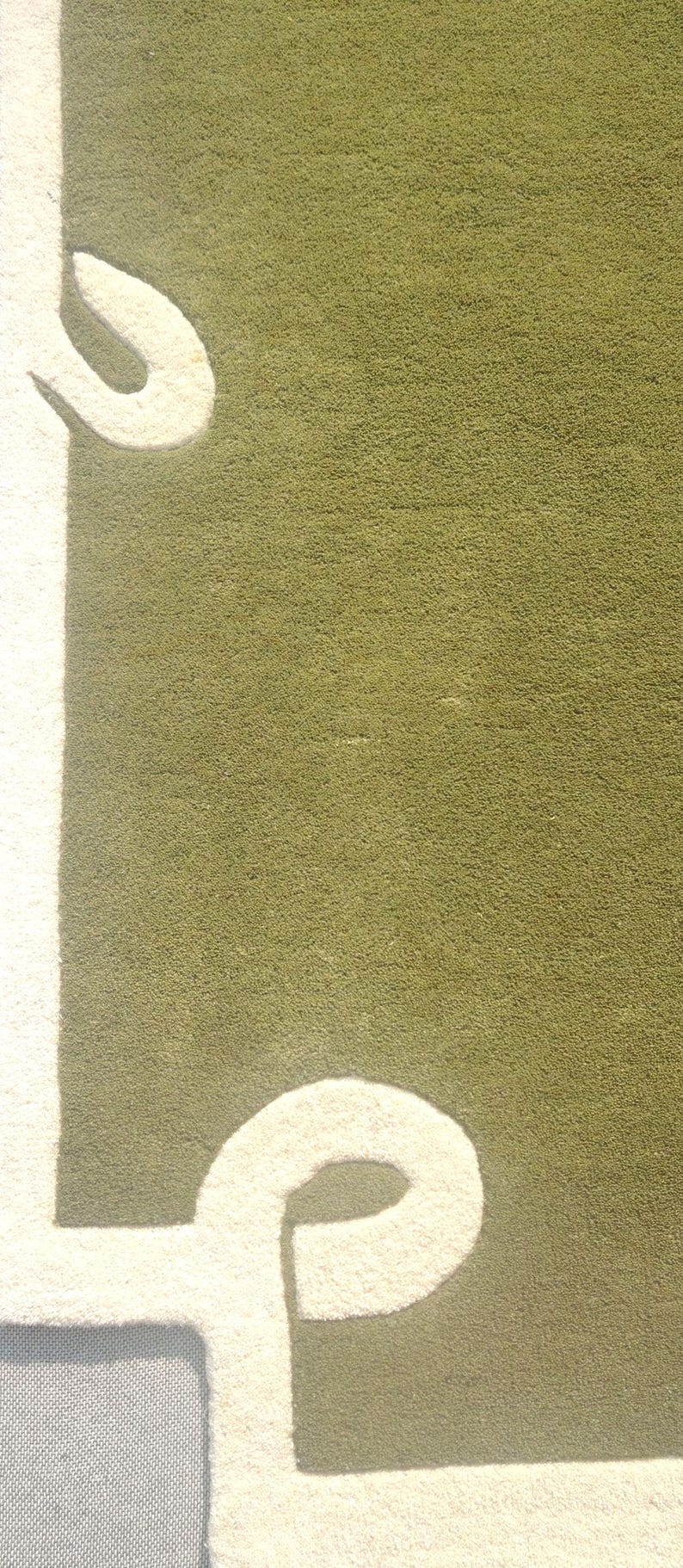 Op de afbeelding: Close-up van een groen tapijt met een witte, gestileerde letter 'P' en een gebogen ontwerp. Het tapijt heeft een getextureerd oppervlak en een rechthoekige vorm. Het ontwerp is een modern, abstract patroon.