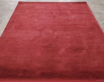 May include: A rectangular, deep red rug with a soft, textured surface. The rug displays subtle variations in tone across its surface. The rug is placed on a concrete floor. The rug's dimensions are in centimetres.