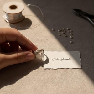 K&ouml;nnte beinhalten: Ein silberner Ring mit Blattdesign wird in der N&auml;he einer Karte mit der Aufschrift "Aelia Jewels" gehalten. Der Ring befindet sich neben einer Spule aus Silberdraht, kleinen Silberperlen und einer Zange. Das Design des Rings ist detailliert und strukturiert.