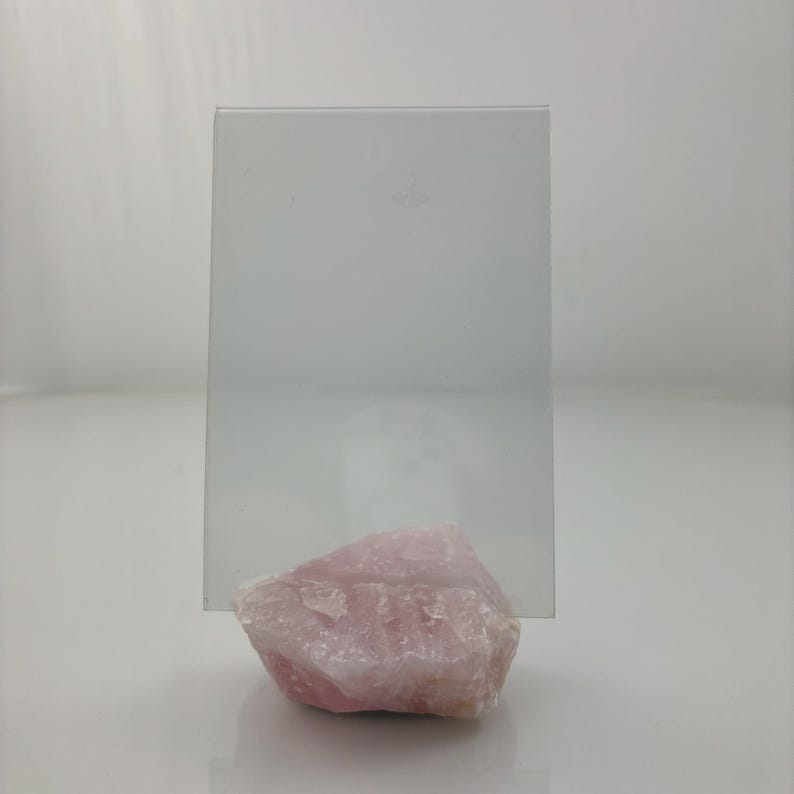 Op de afbeelding: Een helder glazen fotolijstje staat op een grote, roze, natuurlijke kwartskristal.