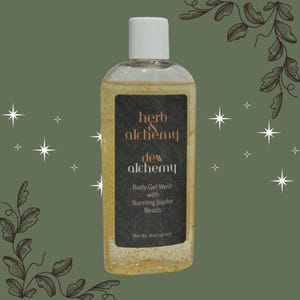 Puede incluir: Una botella de plástico transparente que contiene gel de baño corporal dorado con perlas en suspensión. La etiqueta negra presenta el texto herb & alchemy, dew alchemy, Body Gel Wash with Bursting Jojoba Beads y Net Wt. 8oz/236.5ml con tapa blanca.