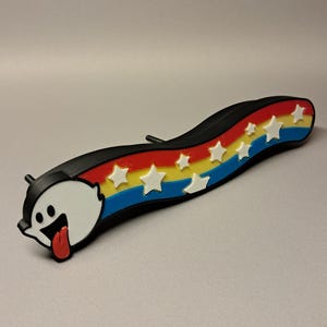 May include: A black, curved decorative item featuring a cartoon ghost with a red tongue and a rainbow design with white stars. The rainbow has red, yellow, and blue stripes. The item is likely a decorative accessory.