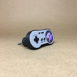 May include: A black and gray Super Nintendo controller-shaped door knob with purple buttons.