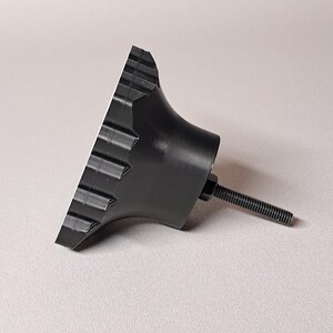 May include: A black knob with a ridged edge and a threaded bolt. The knob has a conical shape with a flat, ridged surface. The bolt extends from the back of the knob.