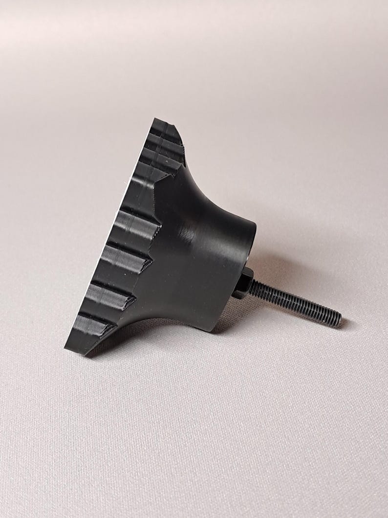 May include: A black knob with a ridged edge and a threaded bolt. The knob has a conical shape with a flat, ridged surface. The bolt extends from the back of the knob.