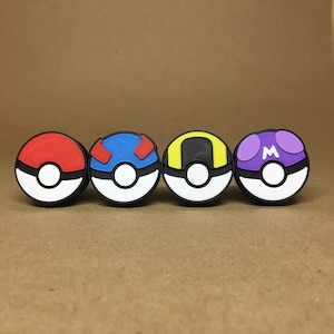 May include: Four Pokeball-style toys, each with a different color and design. The Pokeballs are red, blue, yellow, and purple. Each Pokeball has a black center with a white circle in the middle.
