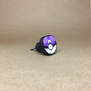 May include: A black and white Pokeball door knob with a purple 'M' on the top.