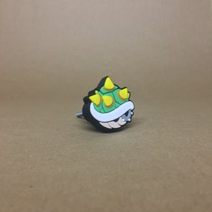 May include: A black and green plastic knob shaped like a spiky turtle shell. The shell has yellow spikes and a white underbelly.