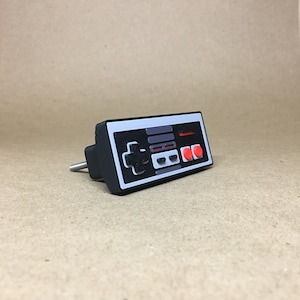 May include: A black and gray plastic door knob shaped like a vintage video game controller with red buttons.