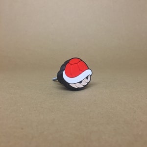 May include: A red and black plastic cabinet knob shaped like a Super Mario Bros. Koopa shell.
