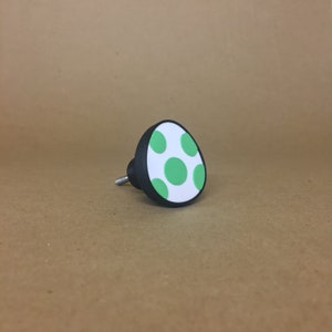 May include: A white and green egg-shaped door knob with a black base. The knob has a green polka dot pattern.