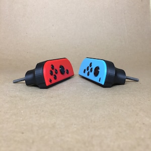 May include: Two 3D printed Nintendo Switch controller shells, one red and one blue, with black buttons and a screw on the side.