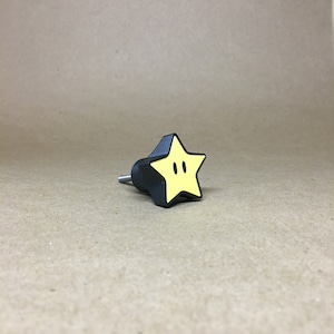 May include: A black star-shaped cabinet knob with a yellow star and two black eyes on the front.