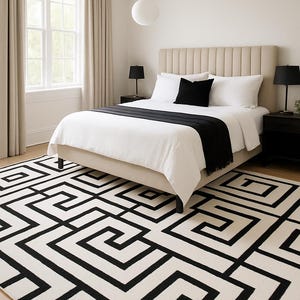 May include: A bedroom scene with a bed featuring a beige headboard, white bedding, and a black throw. The room includes a black and white geometric patterned rug, black bedside tables, and a window with beige curtains. Two black lamps are on the bedside tables.