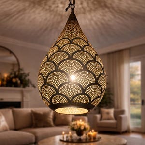 May include: A decorative, teardrop-shaped pendant light fixture with a dark bronze finish. The light has a detailed, openwork design of repeating semi-circles and dot patterns. The light is hanging in a living room.