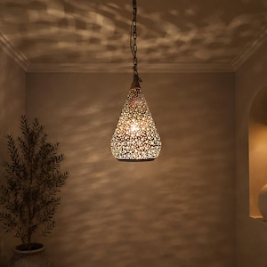May include: A teardrop-shaped metal pendant light fixture with an intricate, perforated pattern that casts complex, dappled light and shadow effects onto the surrounding walls. The lamp hangs from a dark metal chain and emits a warm, golden glow.