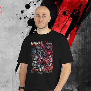 May include: Black t-shirt featuring a graphic design with the word "YOKAI" above a collection of red, gray, and black demon illustrations. The text "DEMONS OF THE INNER MIND" is below the graphic. The shirt is worn by a person.
