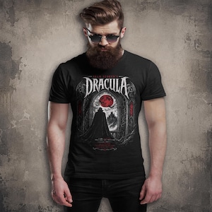 May include: A black short-sleeved t-shirt featuring a graphic print of Bram Stoker's Dracula. The design displays a cloaked figure standing before a gothic archway, a red moon, bats, and a castle silhouette, with white text detailing the movie title.