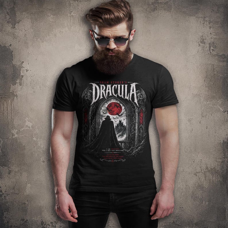 May include: A black short-sleeved t-shirt featuring a graphic print of Bram Stoker's Dracula. The design displays a cloaked figure standing before a gothic archway, a red moon, bats, and a castle silhouette, with white text detailing the movie title.