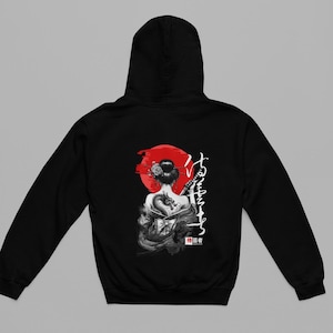 Puede incluir: Sudadera con capucha negra con un gráfico trasero de una geisha con un tatuaje de dragón, sosteniendo una katana frente a un sol rojo. Caracteres japoneses a la derecha. La sudadera tiene capucha y mangas largas.