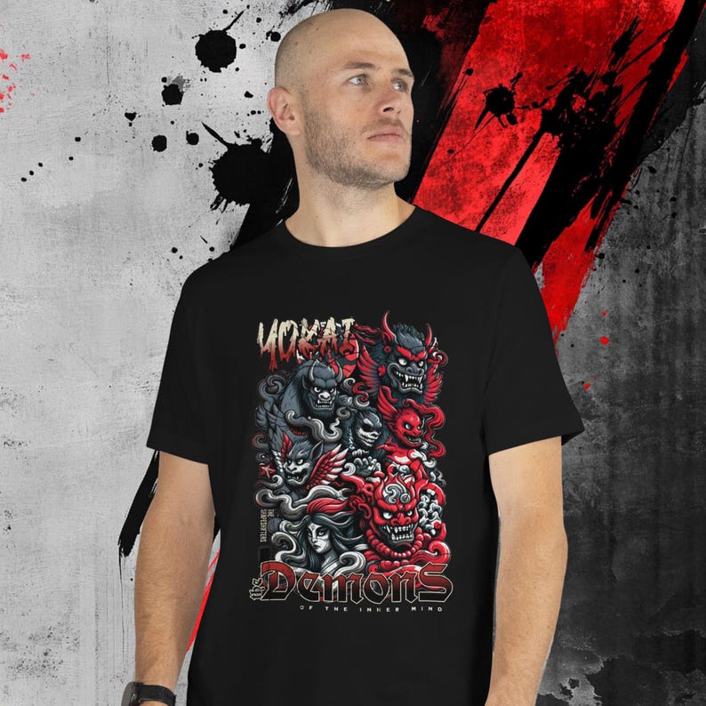 May include: Black t-shirt featuring a vibrant graphic of stylized demons in red, gray, and black. The design includes the word "YOKAI" at the top and "Demons of the Inner Mind" at the bottom. The shirt is worn by a person.