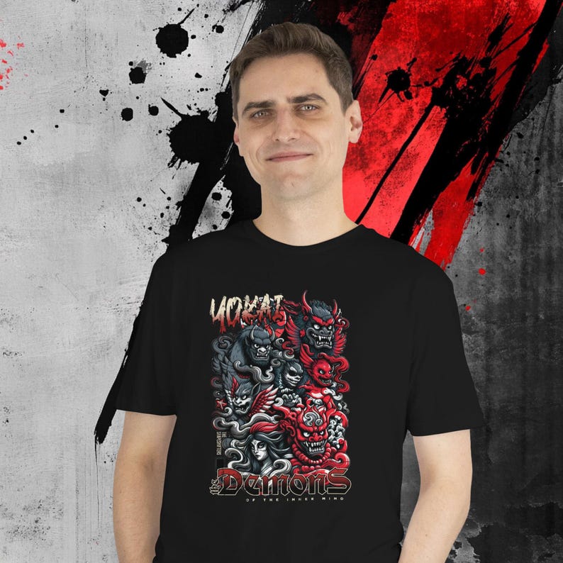May include: Black t-shirt featuring a colorful graphic of demons with the text "YOKAI" and "Demons of the Inner Mind". The design includes red, black, and gray elements. The shirt is worn by a person.