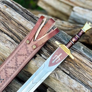 May include: A brown leather scabbard with intricate stitching and a silver sword with a gold hilt and a decorative shield on the blade.