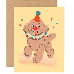 May include: A greeting card featuring a cartoon poodle dressed as a clown. The poodle has a red nose, a party hat, and a ruffled collar. Colorful stars surround the dog on a yellow background. The card is paired with a brown envelope.