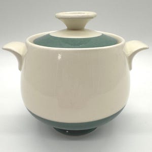May include: Cream-coloured ceramic lidded serving dish with a teal band around the base and lid. The lid has a teal stripe and a small, off-white knob. The dish has two curved handles on either side.