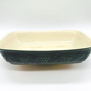 May include: A rectangular baking dish with a cream-colored interior and a dark forest green exterior. The outer sides feature a raised, embossed pattern of grape clusters and vine leaves wrapping around the entire perimeter of the ceramic vessel.
