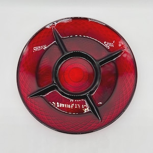May include: A red glass serving dish with a black centre and dividers. The dish has a circular shape with a textured surface and a glossy finish. The centre section is a darker shade of red.