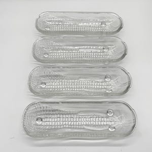 May include: Four clear, rectangular glass dishes with textured interiors and rounded ends are arranged vertically. Each dish has a small, circular indentation near the center and a subtle, curved design at the ends. The dishes are transparent, allowing light to pass through.