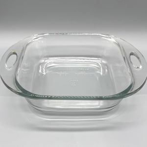 May include: A clear, square glass baking dish with rounded handles on each side. The dish has a slightly curved rim and appears to be empty. The interior has measurement markings.