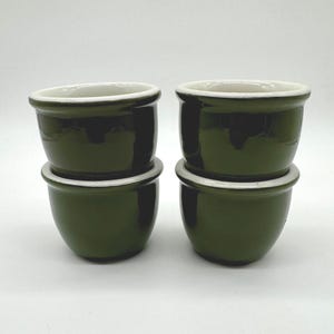 May include: Four small, dark green ceramic bowls stacked in pairs. Each bowl has a white rim and a glossy finish. The bowls are likely for serving individual portions of food.