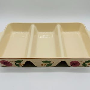 May include: A rectangular ceramic serving dish with three separate compartments and integrated side handles. The interior is a solid cream color, while the exterior features a hand-painted pattern of purple plums with green leaves along the base.