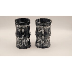 May include: Two black and white marble cups with a bamboo design. The cups are cylindrical and have a smooth, polished finish.