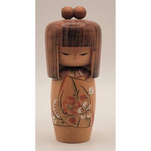 May include: A wooden Japanese Kokeshi doll with a rounded head and a cylindrical body. The doll features a brown hair design, closed eyes, and a floral pattern in red, white, and green on the body. Two small wooden spheres are on top of the head.