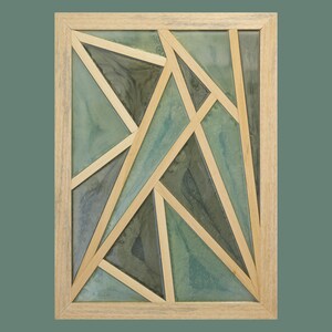 Peut inclure: Œuvre d'art murale abstraite avec un design géométrique. L'œuvre est encadrée de bois clair et présente un fond aux teintes de vert d'eau, de vert et de gris. De fines lattes de bois clair forment le motif géométrique.
