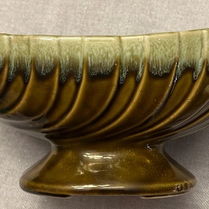 Könnte beinhalten: Eine Vintage-Keramikschale mit Sockel. Die Schale hat eine gebogene, längliche Form mit geriffelter Außenseite. Der Farbverlauf geht von einem hellen Grün oben zu einem dunklen Braun an der Basis über. Der Sockel ist ein dunklerer Braunton.
