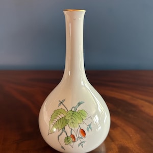 May include: A white ceramic vase with a bulbous base and a slender neck. The vase features a botanical design of green leaves and red berries. The rim is trimmed with gold. The vase is likely for decorative purposes.
