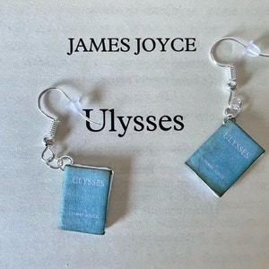 Può includere: Orecchini pendenti color argento con ciondoli a forma di libro in miniatura. Ogni ciondolo è un rettangolo azzurro con il titolo "Ulysses" e il nome dell'autore, "James Joyce". Gli orecchini hanno un semplice design a gancio.
